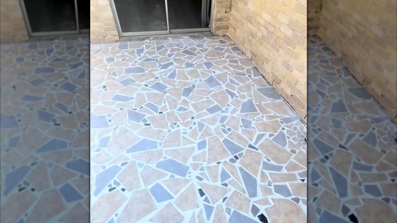 A random mosaic tile pattern covers the concrete patio of a brick house
