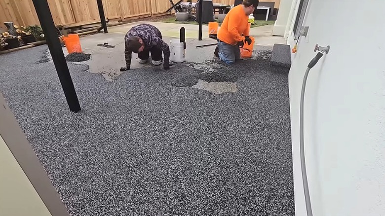 Workers troweling rubber coating onto concrete patio