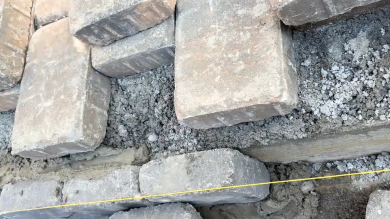 A yellow guideline is shown near inexpensive pavers set into gray mortar mix