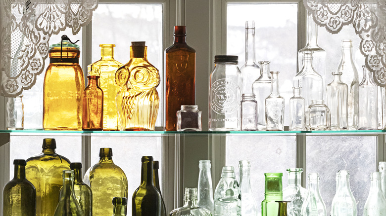 Old-fashioned bottles on glass shelves in front of a window with a white lace curtain