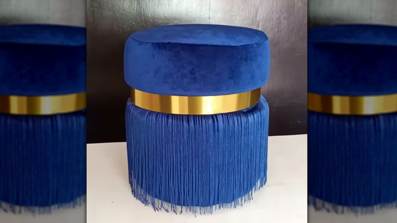Blue velvet ottoman covered in fringe, with gold band, made from a bucket.