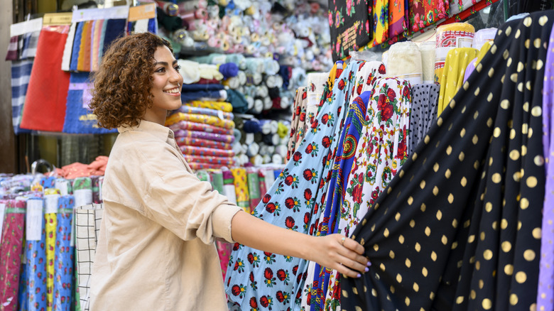 A smiling woman looks at bolts of fabric