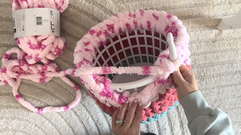 Person covering a laundry basket in different chunky yarns