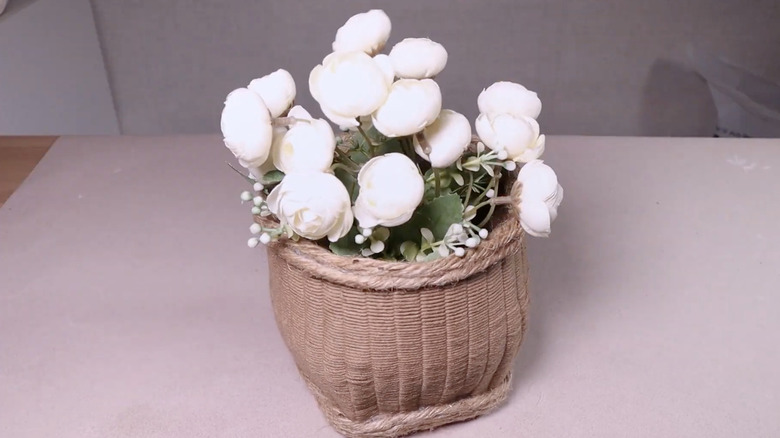 Brown woven vase on a table with faux flowers in it