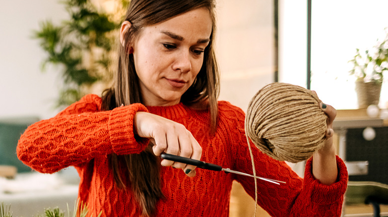 A woman uses scissors to cut a piece of rope from a ball of twine