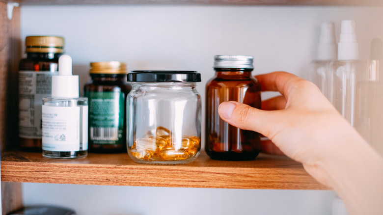Unidentified woman's hand reaching for a pill bottle in a medicine cabinet
