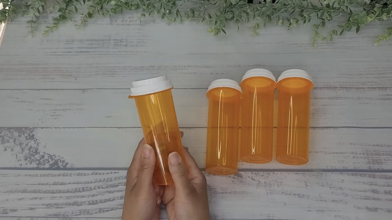 A person holding four empty pill bottles, ready to use for a craft project.