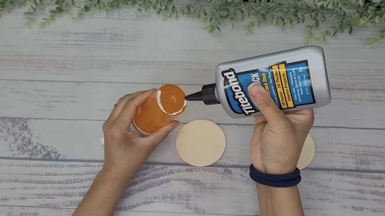A person applying glue to the bottom of the pill bottle to affix the base.