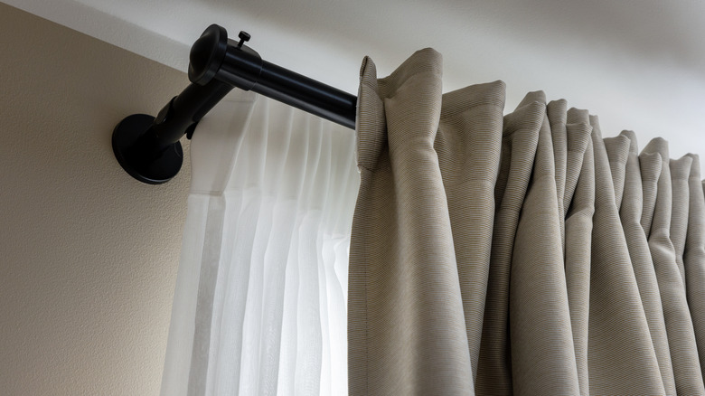 A dual curtain rod with a sheer curtain panel behind a beige curtain panel