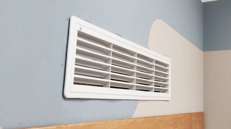 Air vent on a patterned white and blue wall with a wooden baseboard