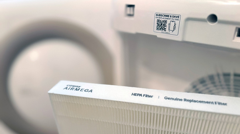 A QR code sticker reading "Subscribe & Save" is on a Coway Airmega Mighty in front of a replacement HEPA filter