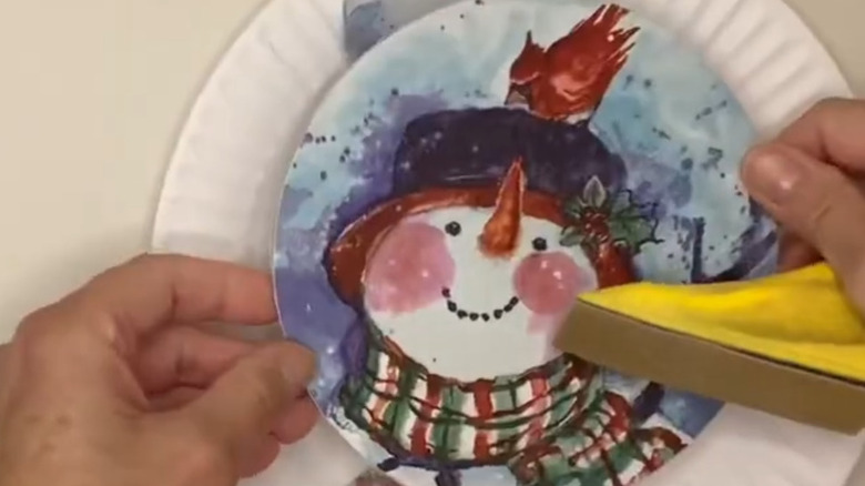 A woman decoupaging a snow man onto a wood circle