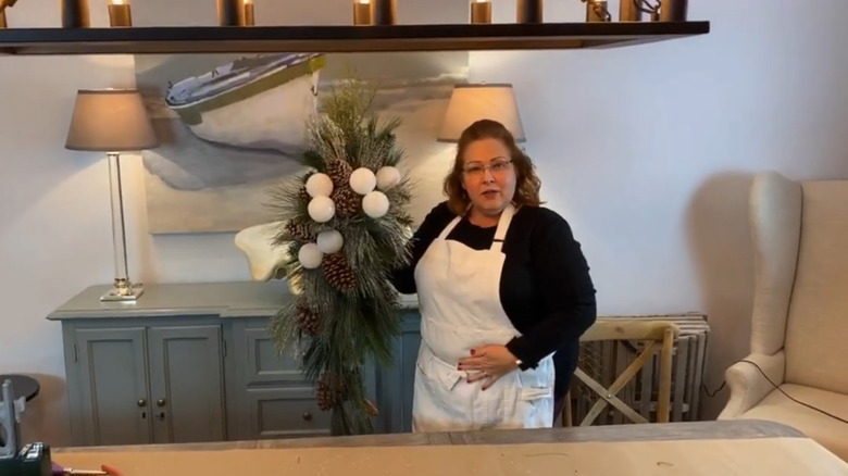 Woman holding front door decor made of styrofoam snowballs and pine branches