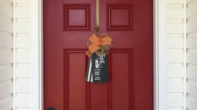 A gift tage shaped door hanger with an orange ribbon and the phrase trick or treat painted on it