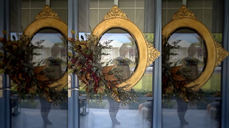 A gold picture frame decorated with seasonal foliage hanging on a door