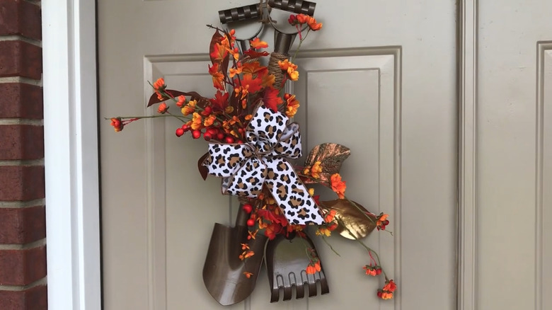 A door with a small shovel and rake mounted on the front, tied together with ribbon and fall plants
