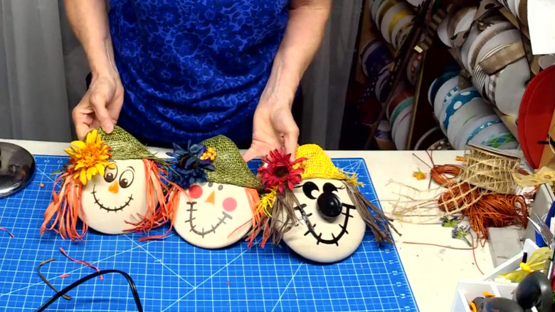 A woman holding three pot lid scarecrows