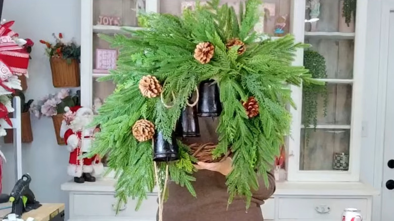 A woman holding a wreath of pine branches, black metal bells, and pine cones