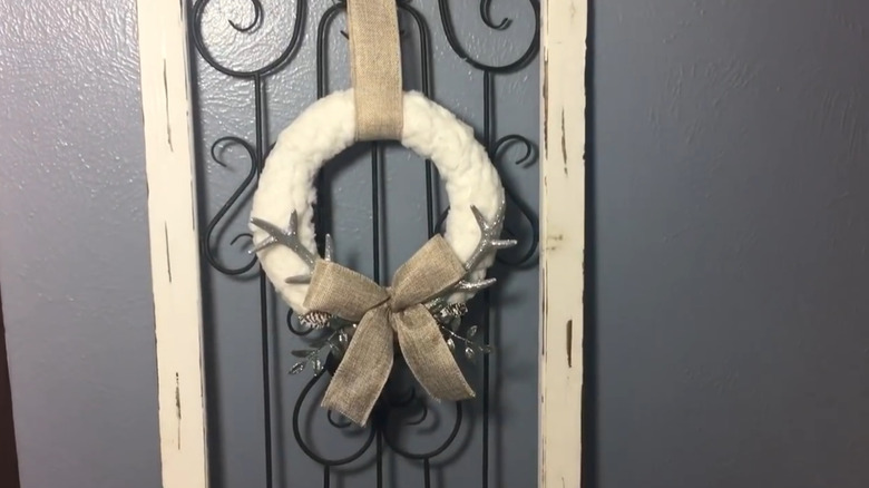 A white faux fur wreath with silver faux antlers and brown ribbon