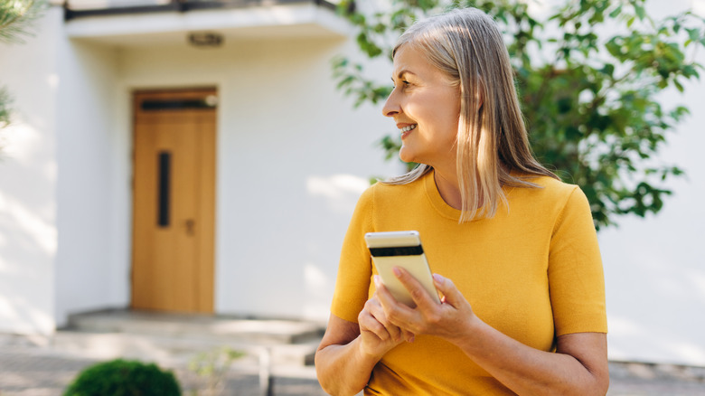 A woman browses on her phone while standing outside her house