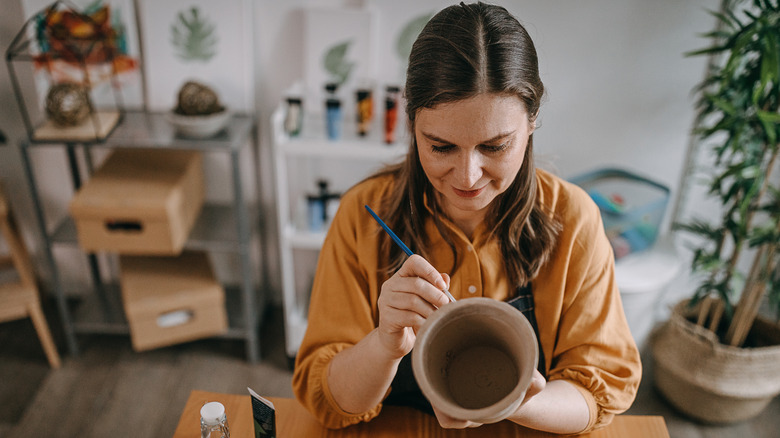 A woman smiles and paints a clay pot in a craft room
