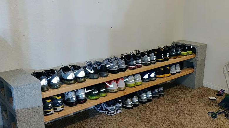 A shoe rack made of concrete blocks and wood boards with a line of sneakers across it