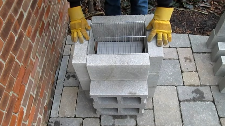 Person fitting a grill grate into a concrete block grill