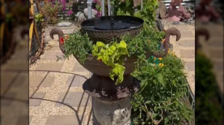 a planter with a fountain on top and plastic flamingo heads on the sides