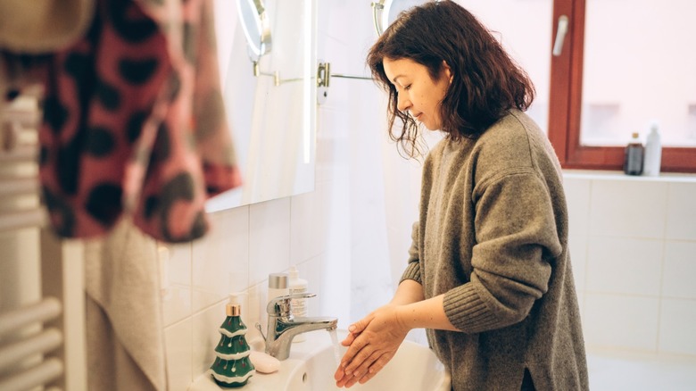 Woman washing hands in sink in small bathroom