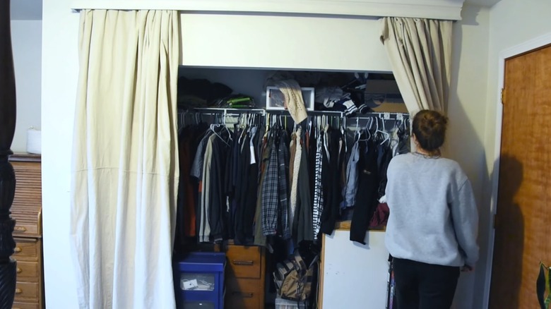 Young woman standing in front of cluttered closet with thick off-white drapes for doors