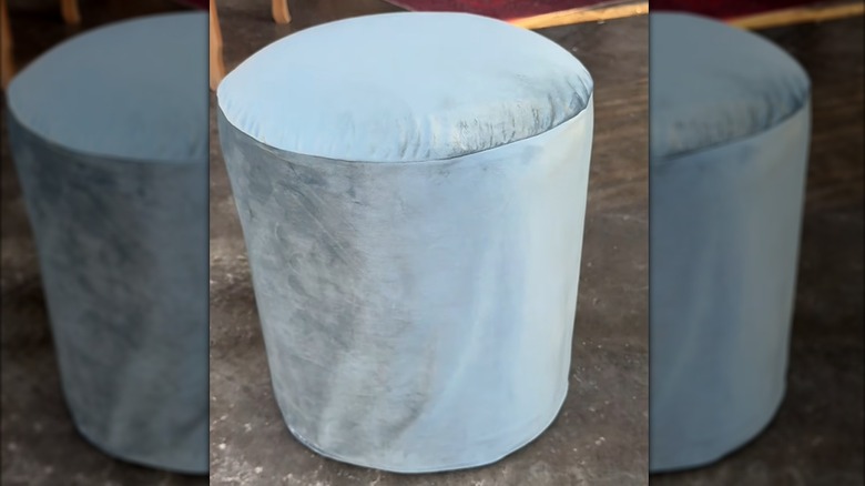 Light blue ottoman with velvet drape slipcover on concrete floor