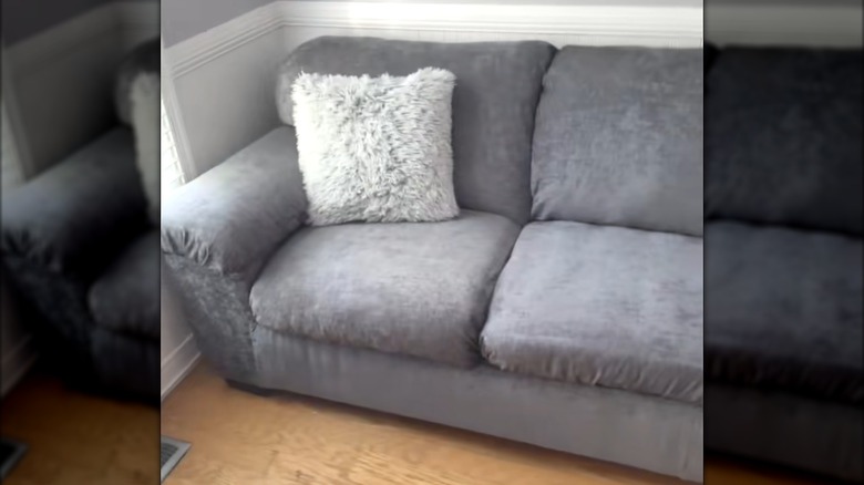 Gray couch with velvet slipcover and fluffy white throw pillow on wood floor