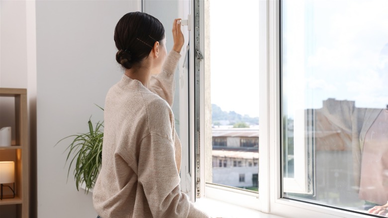 Woman opening window looking out into neighborhood