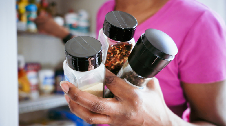 Woman holding bottles of spices in front of a pantry