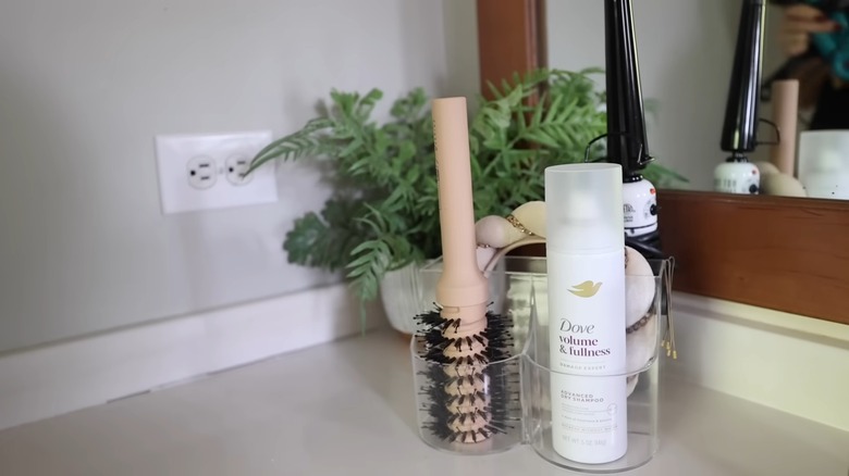 Hair tools and accessories inside a clear countertop organizer with bobby pins hanging on the side