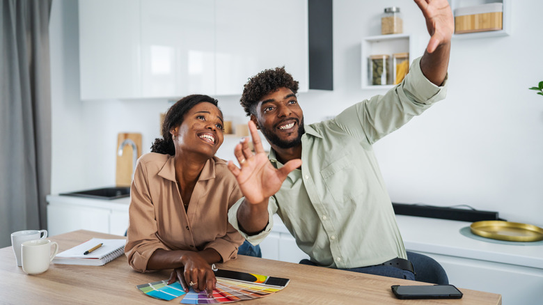 A smiling couple looks as paint swatches as they decide how to paint their dining room