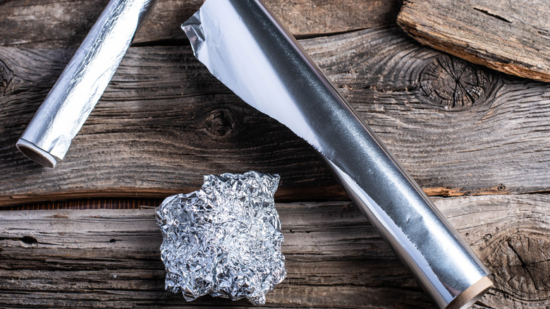 Two rolls of aluminum foil and a crumpled aluminum foil ball on a wooden table