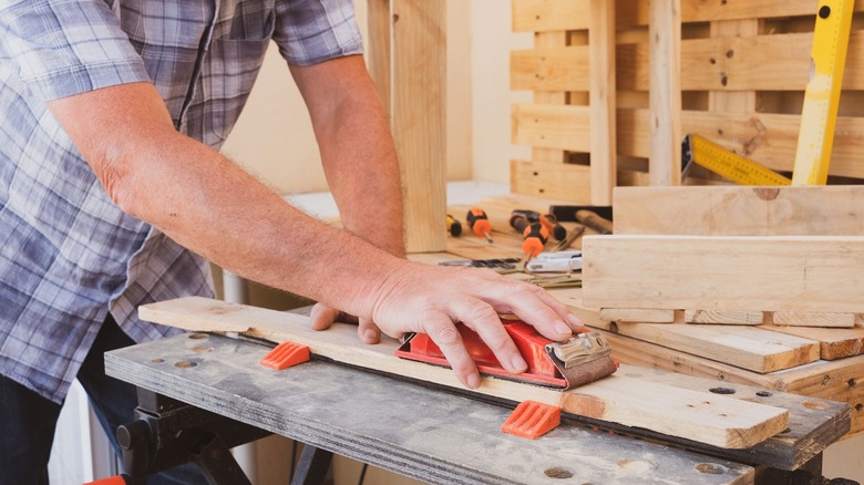 Person sanding repurposed broken-down pallets in workshop