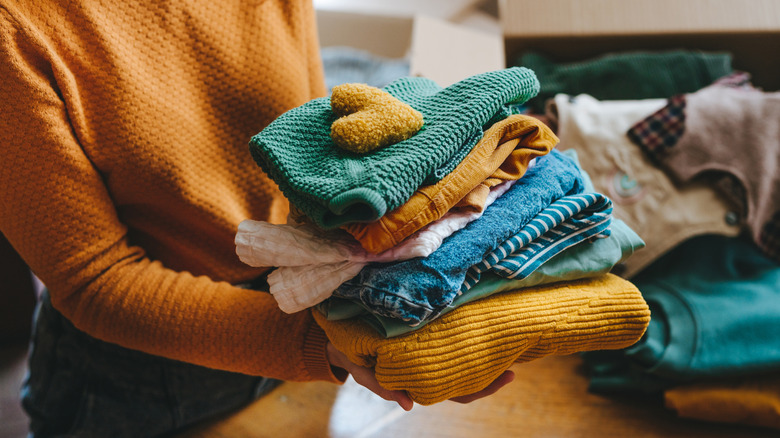 Person sorting clothes and holding a stack of bulky items
