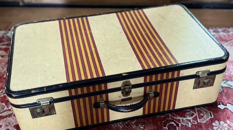 An Oshkosh yellow and red striped vintage suitcase on a red rug