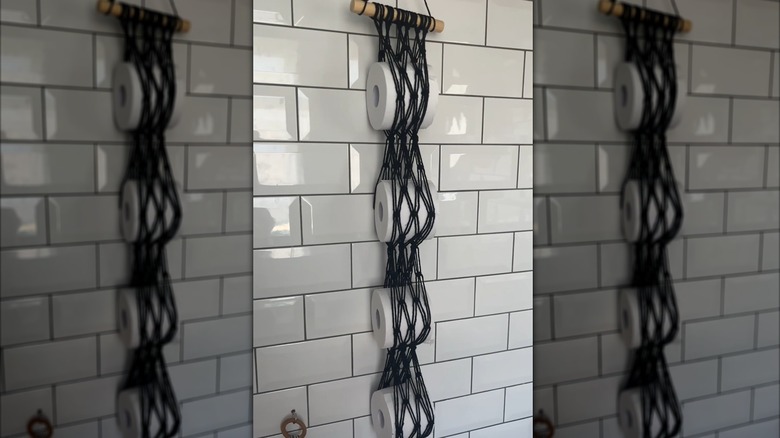 Macrame toilet paper holder hanging on a wall with four rolls in it