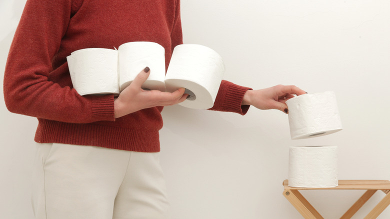 Person bringing several rolls of toilet paper into the bathroom