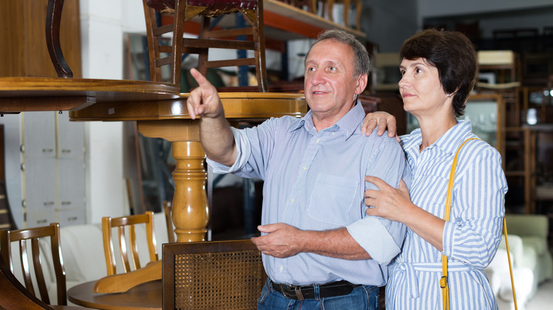 A couple shopping in a thrift store, with the main pointing at an item
