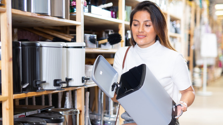 Woman holding bathroom trash can in garbage can aisle of store