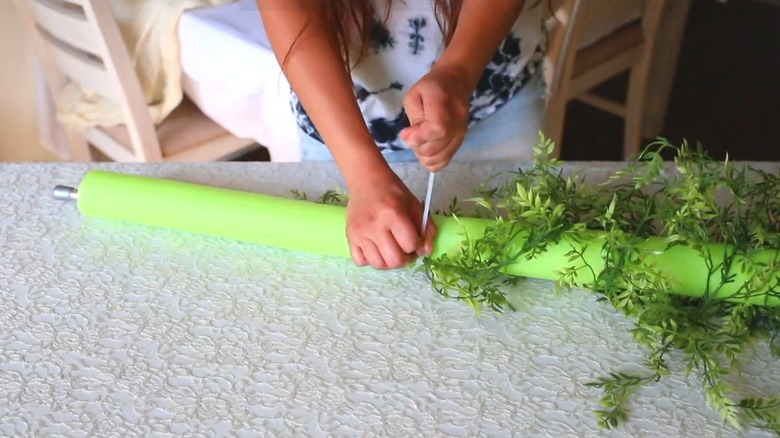 Woman wrapping green pool noodle in green garland with a zip tie for an interior decor DIY project