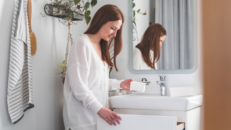 Young woman standing in front of open drawers of counter and taking out toiletries from drawer.
