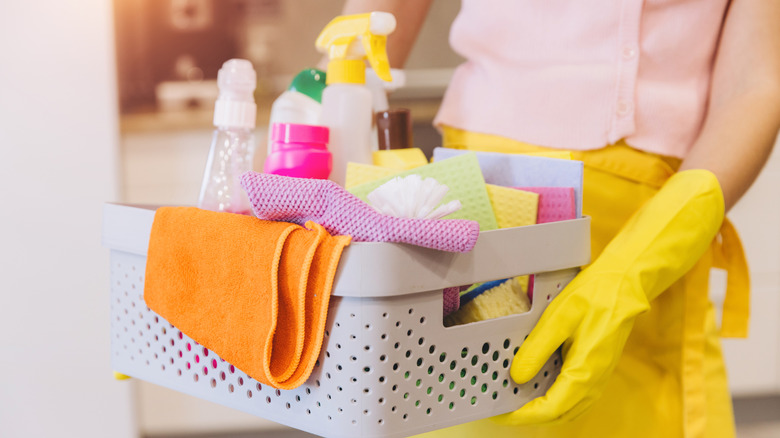 Woman in yellow rubber gloves carrying cleaning products in caddy