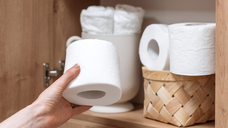 Hand reaching for toilet paper in wooden cabinet with towels and baskets