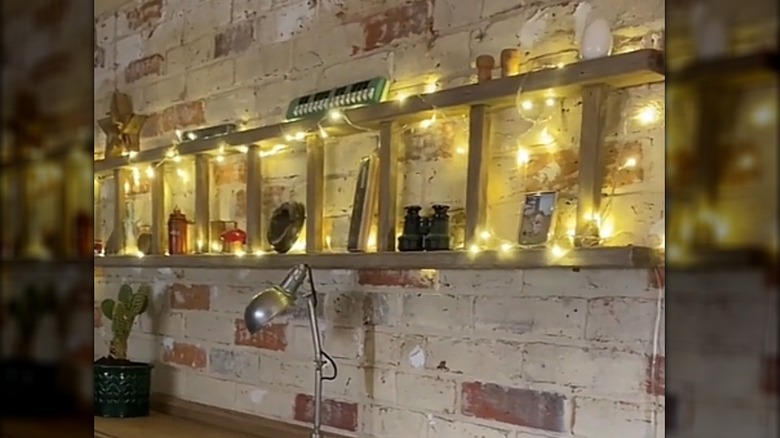 Ladder hung horizontally on the wall with string lights wrapped around it and decor pieces on display