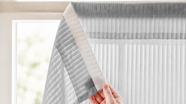 A person hangs up a sheer adhesive curtain in a window.